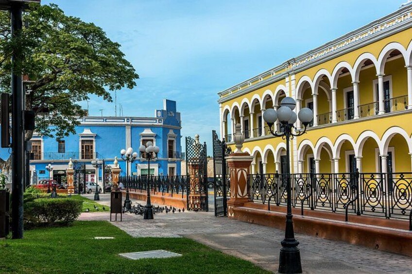 A courtyard with a yellow building with arches, a blue building, and a tree. 5