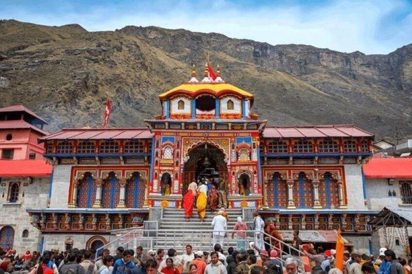 A colorful temple with intricate architecture, a crowd of people, and a mountainous backdrop. 2