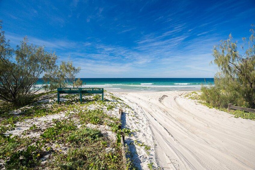 A beach with a sign indicating camping areas, a sandy path, and ocean view. 4