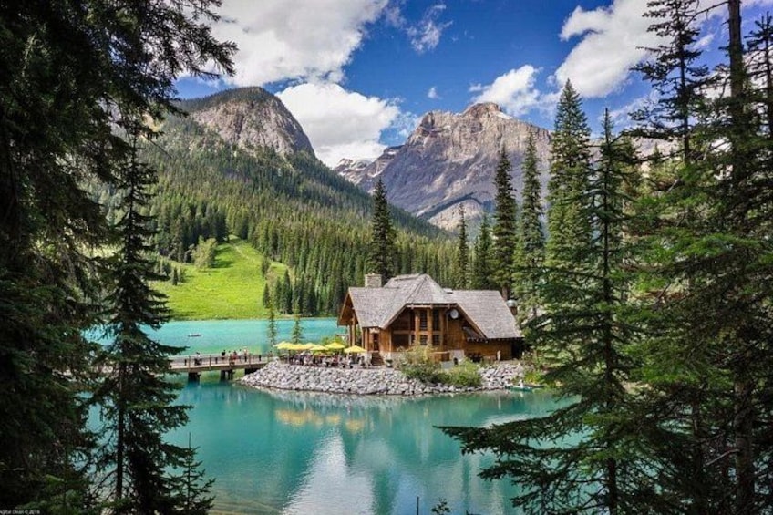 A cabin by a turquoise lake surrounded by pine trees and mountains. 4
