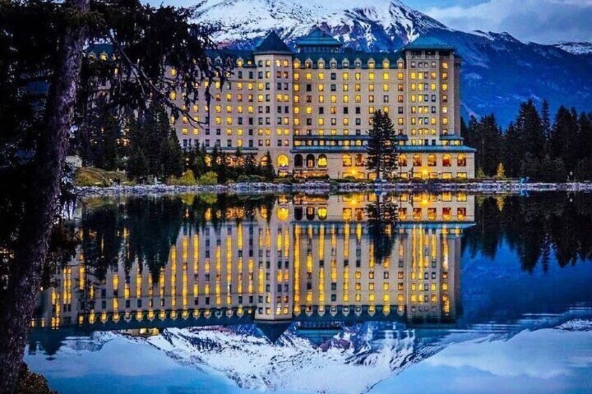 Ein großes, beleuchtetes Hotel mit Spiegelung in einem ruhigen See, umgeben von schneebedeckten Bergen. 2
