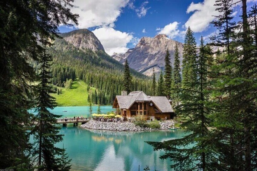 Eine Holzhütte an einem türkisfarbenen See, umgeben von Kiefern und Bergen. 4