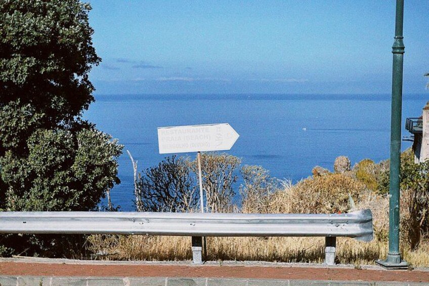 A coastal road sign with a view of the sea and a bench in the foreground. 3