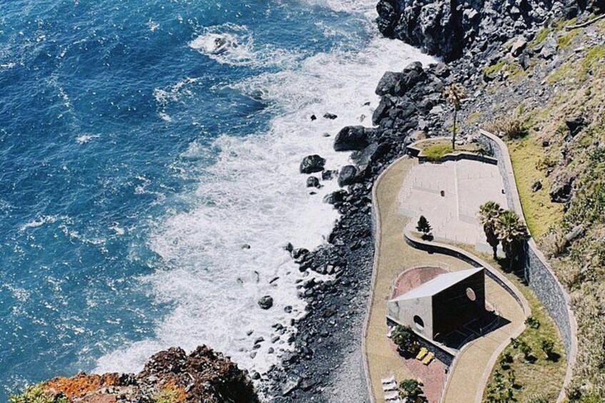 A coastal area with a paved walkway, rocky shoreline, and a building with a dark roof. 2