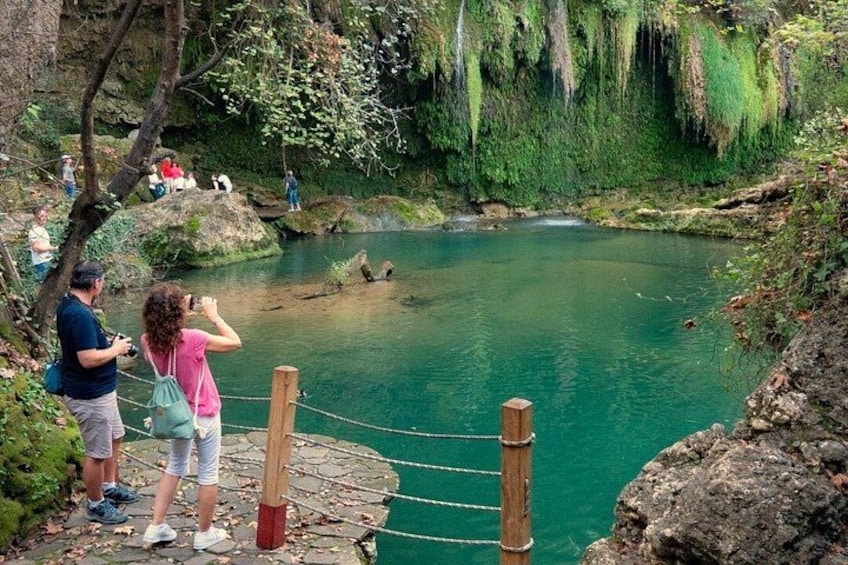 A natural pool surrounded by greenery, with people taking photos and a rope barrier. 2