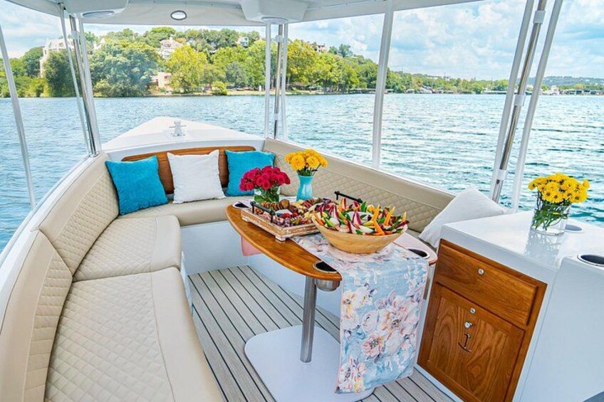 A boat interior with a cushioned seating area, a table with flowers, and a view of a lake. 4