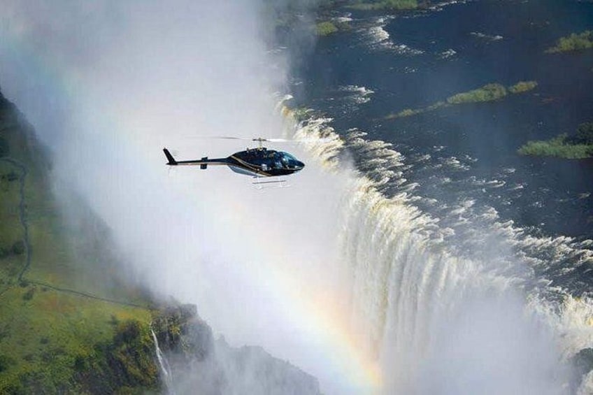 A helicopter flying over a waterfall with a rainbow. 4