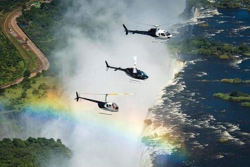 Three helicopters flying over a coastal area with a visible rainbow. 1
