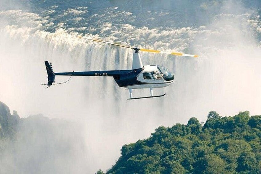 A helicopter flying over a waterfall with a forested area below. 2