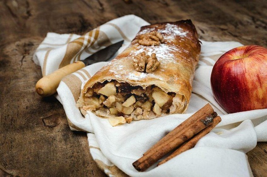 A pastry with walnuts and diced apples, a cinnamon stick, and an apple on a wooden surface. 4