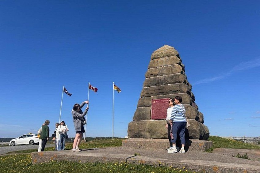 Een stenen monument met vlaggen, een heldere lucht en uitzicht op de kust. 3