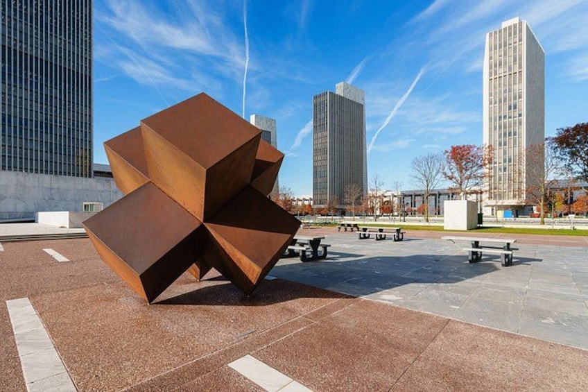 Een moderne sculptuur op een openbaar plein, met hoge gebouwen op de achtergrond. 3