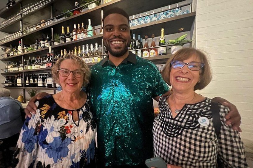 Three people standing in a bar with shelves of bottles in the background. 3