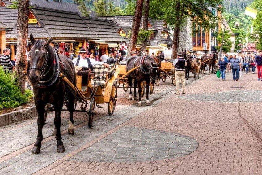 A cobblestone street with horse-drawn carriages and pedestrians. 3