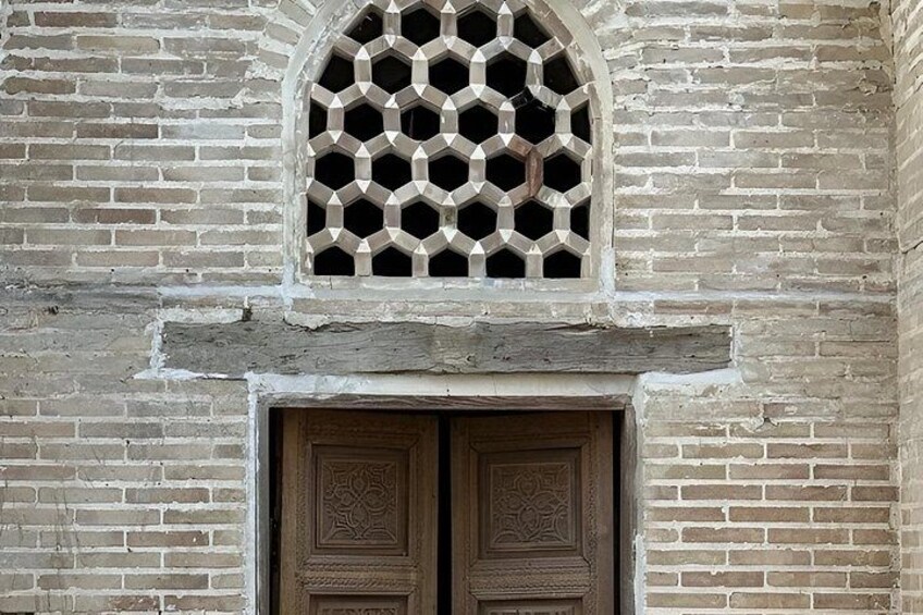 A brick wall with a wooden door and a window with a geometric pattern. 4