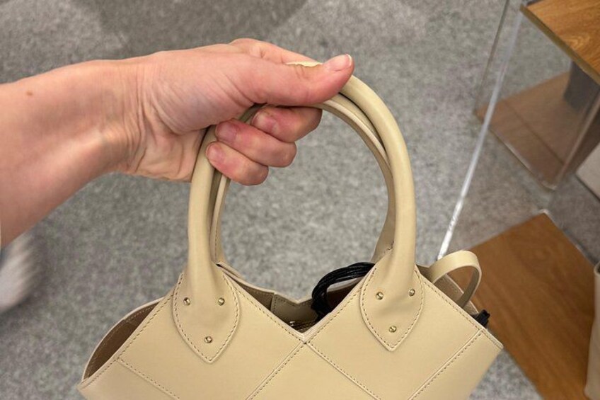 Una mano sosteniendo un bolso beige con asa. 4
