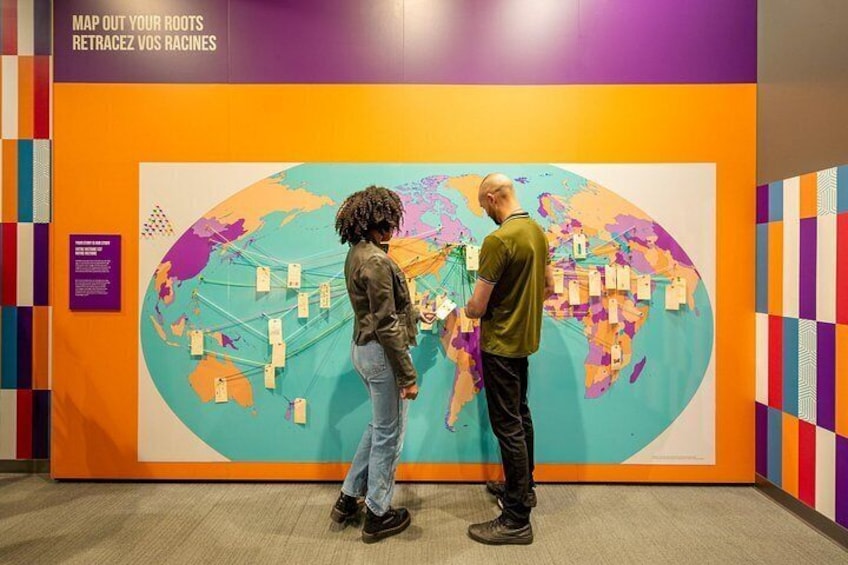 Two people examining a large world map with pins and strings, in a room with colorful walls. 2