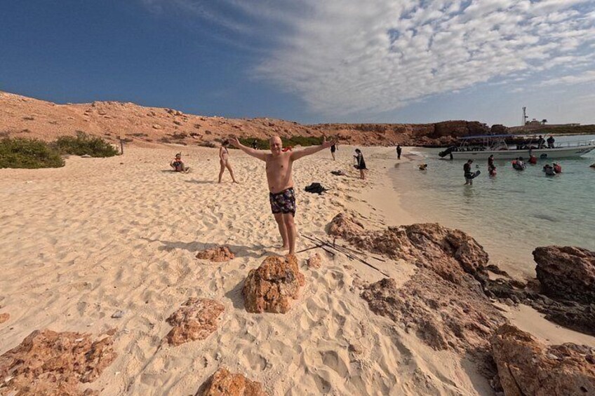 A beach with people sunbathing and swimming, rocky terrain, and clear skies. 4