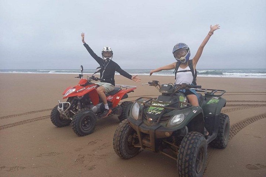 To personer kører på ATV'er på en sandstrand med hav i baggrunden. 3