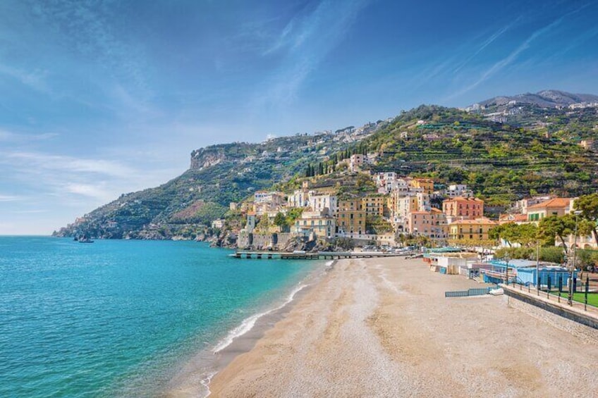 A coastal town with a beach, buildings, and a hillside. 1