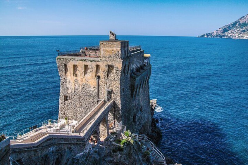 A stone tower with a staircase leading down to the sea, overlooking a clear blue ocean. 2