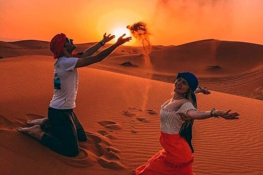 To personer danser i en ørken med sandklitter og en solnedgang i baggrunden. 2