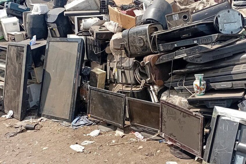 A pile of discarded electronic devices, including televisions and monitors, in a cluttered outdoor setting. 2