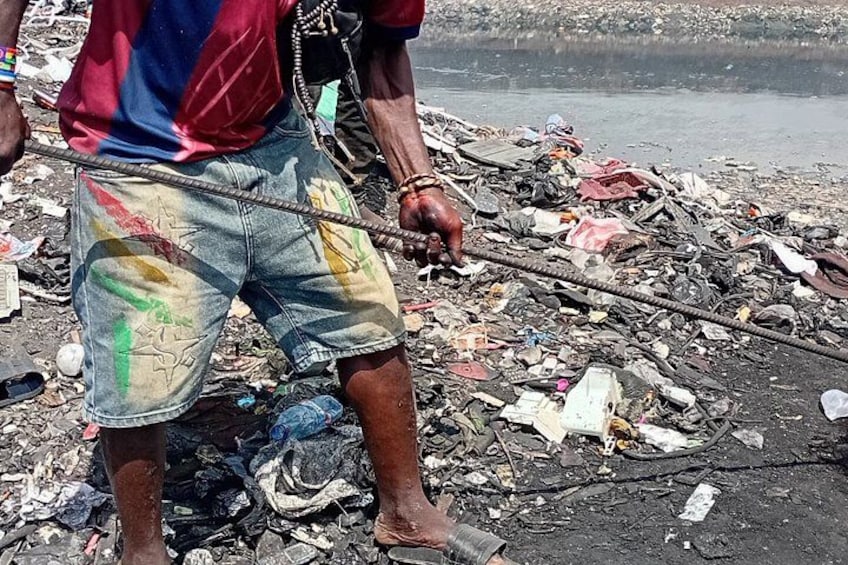 A person standing on a polluted shoreline with debris and trash. 4
