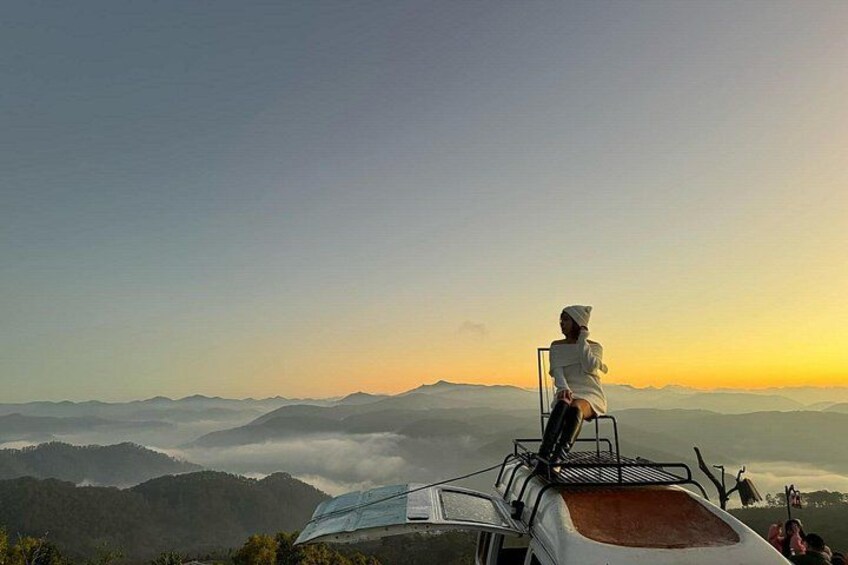 Eine Person sitzt auf einem Stuhl und blickt auf eine gebirgige Landschaft im Morgengrauen. 5