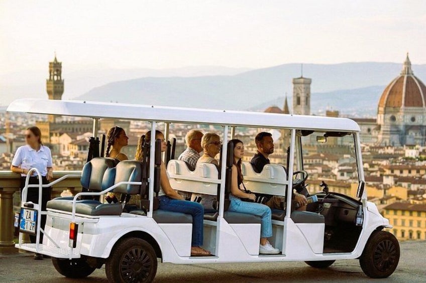 Un carrito de golf blanco con pasajeros, un paisaje urbano con una cúpula destacada al fondo. 2