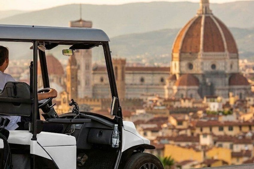 Un carrito de golf con una persona adentro, con vistas a un paisaje urbano y un edificio de cúpula destacada al fondo. 1