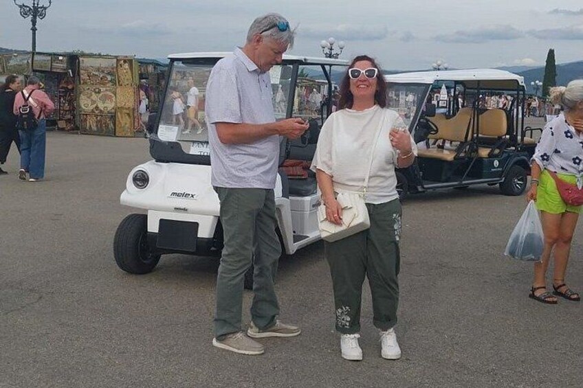Dos personas de pie frente a un carrito de golf, con otro carrito de golf al fondo. 4