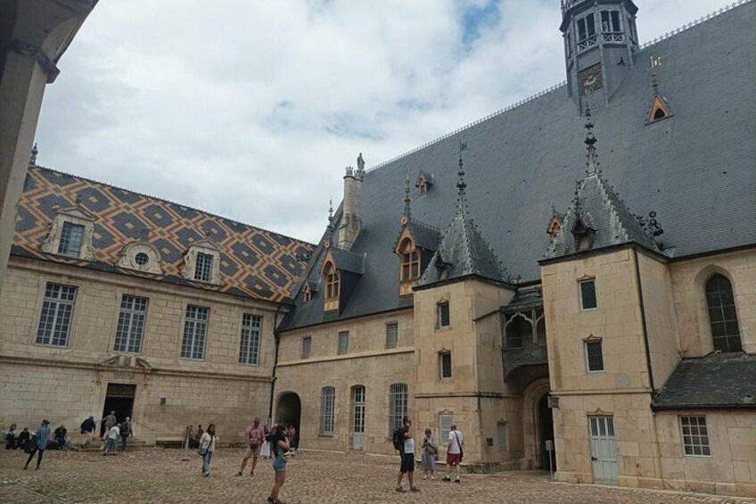 Un edificio histórico con tejado adornado, una torre de reloj y un patio con gente. 3