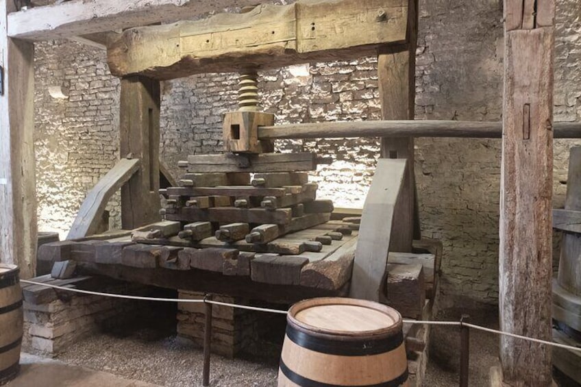 Une vieille presse en bois, dotée de pièces métalliques, adossée à un mur de pierre. 5
