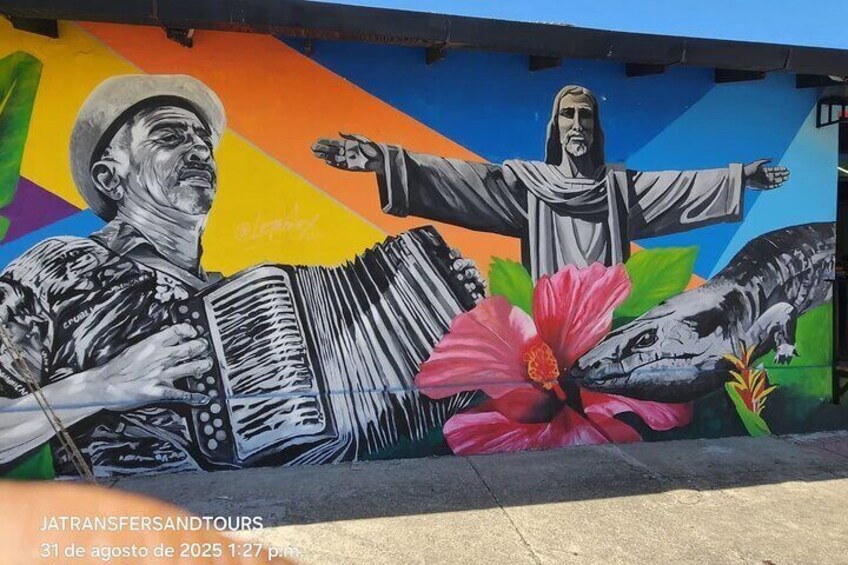 A mural with a person playing an accordion, a figure with outstretched arms, and a large pink flower. 1