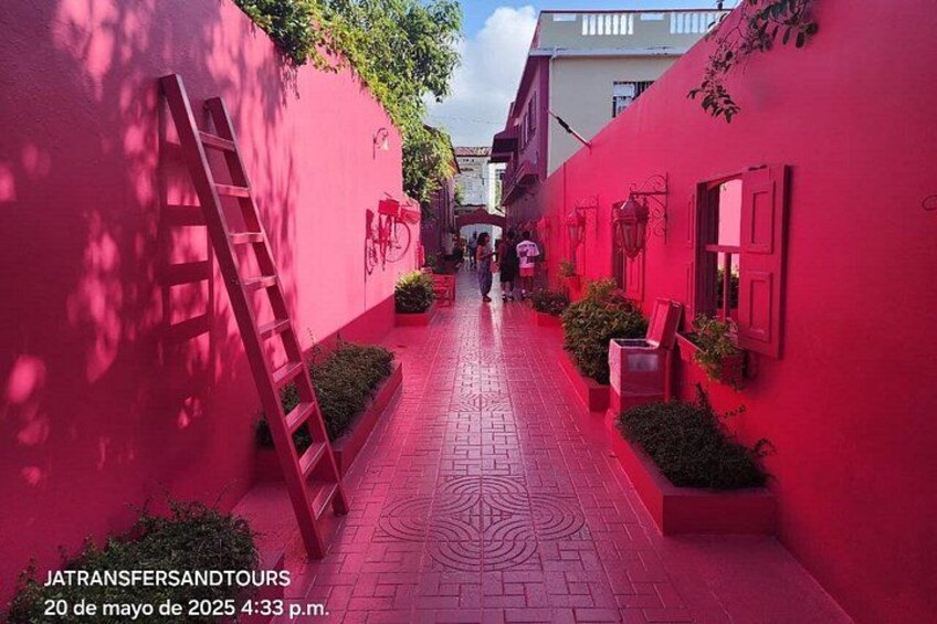 A narrow alley with red walls, a ladder, and a few people walking. 2