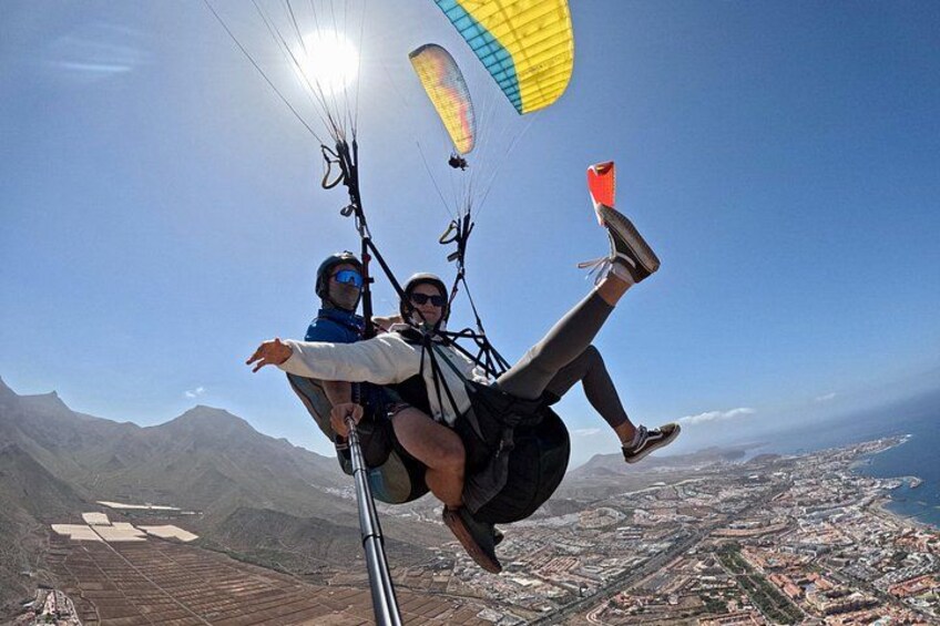 En person paraglider med faldskærm, en anden person holder i en kontrolstang, og en byudsigt ses nedenfor. 1