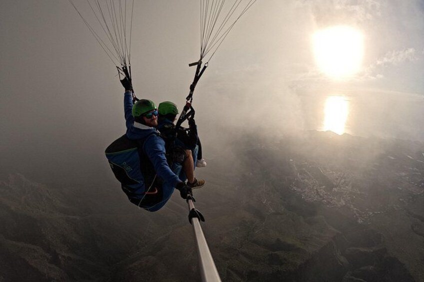 En person paraglider med en faldskærmsele, en klar himmel og et bjergrigt landskab nedenfor. 3