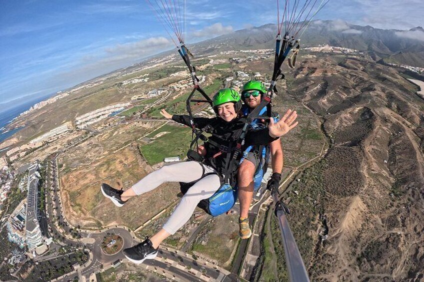 Deux personnes pratiquent le parapente au-dessus d’un paysage comprenant des bâtiments et des montagnes. 4
