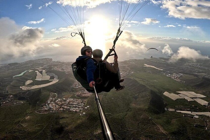 Une personne pratiquant le parapente au-dessus d’un paysage comprenant des bâtiments et des champs. 3