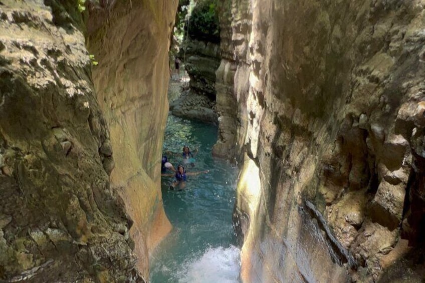 A narrow canyon with a river flowing through it and people swimming in the water. 4