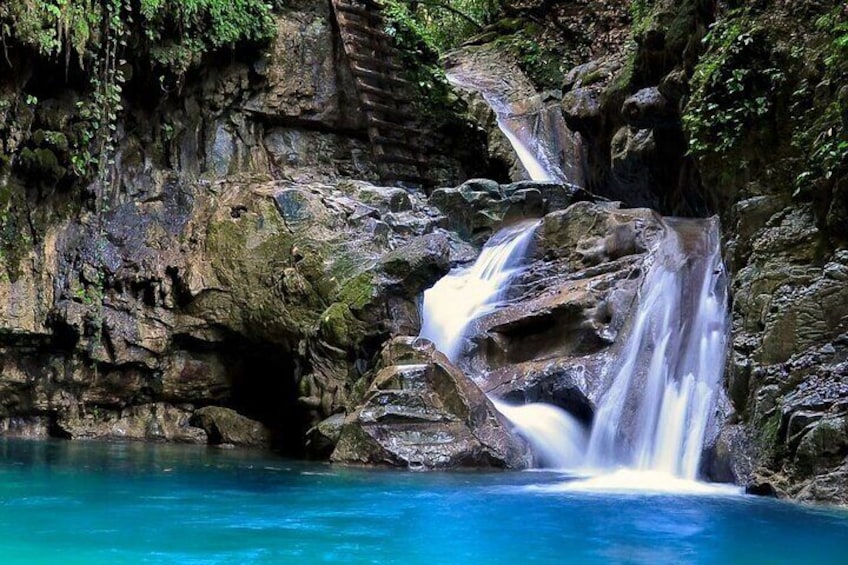 A waterfall cascading over rocks into a turquoise pool surrounded by lush greenery. 1