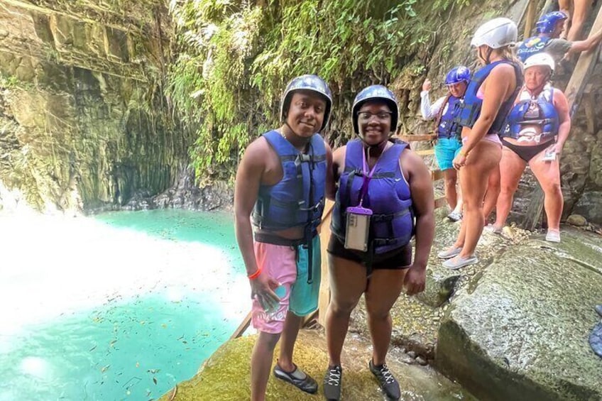 Two people in life vests and helmets near a turquoise pool surrounded by rocky cliffs. 5