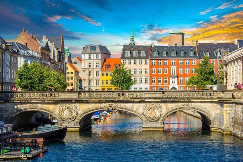 A stone bridge over a river with colorful buildings on the opposite bank. 1