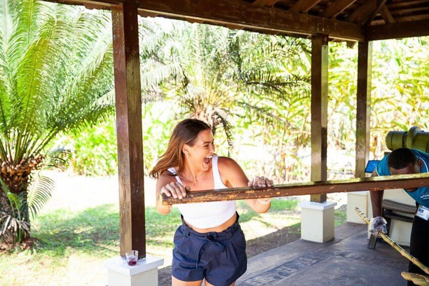 A person holding a wooden beam, standing under a wooden structure with a garden in the background. 1