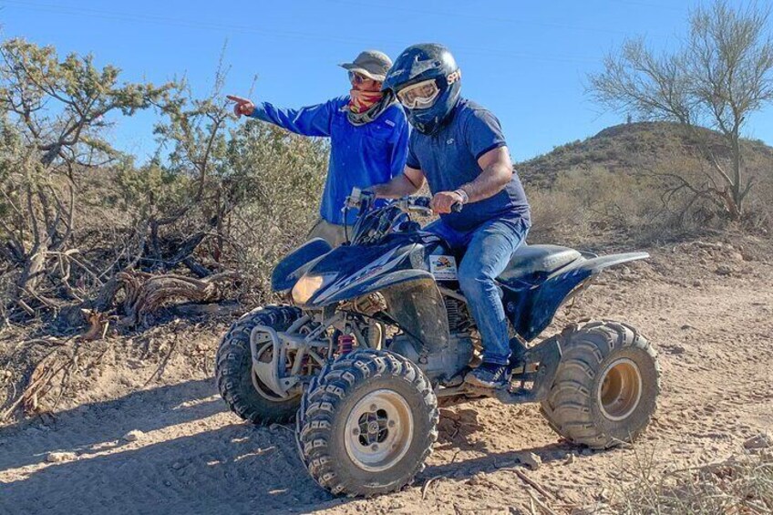 Dos personas en un vehículo todo terreno en un desierto con poca vegetación y cielo despejado. 5