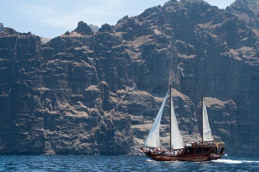 A traditional sailing boat with two sails on a calm sea, surrounded by rocky cliffs. 3