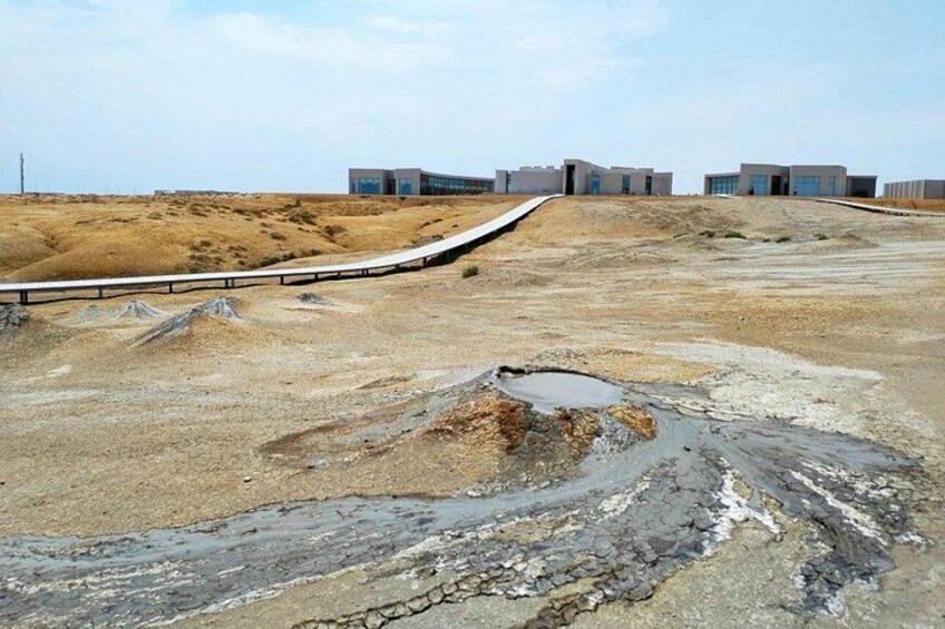 Paisaje desértico con una carretera pavimentada, una barandilla y edificios modernos al fondo. 2