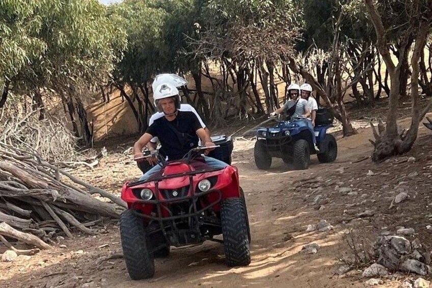 Twee personen rijden op quads over een zandpad, omringd door bomen. 3
