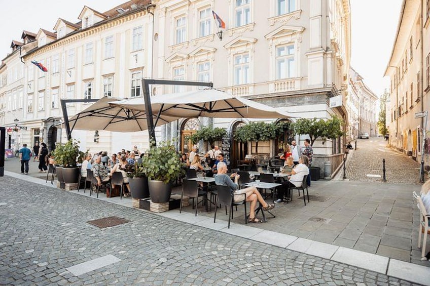 Terrasse de café en plein air, avec tables et parasols, entourée d’immeubles. 1